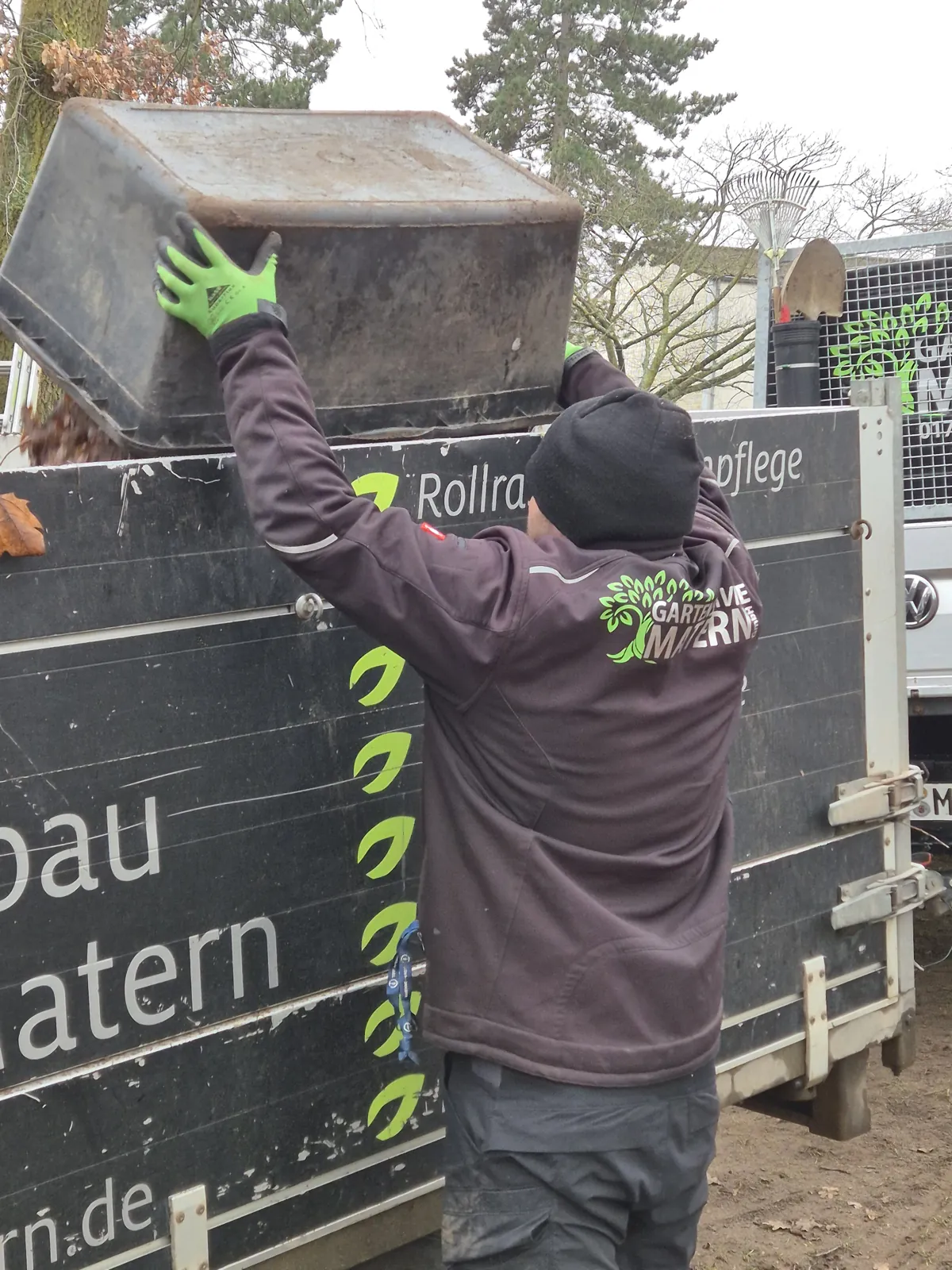 Mitarbeiter von Gartenservice Matern am beschrifteten Firmenanhänger auf der Baustelle